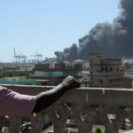 A thick column of black smoke rises above Port Sudan after drone strikes, symbolizing the city's growing humanitarian crisis.