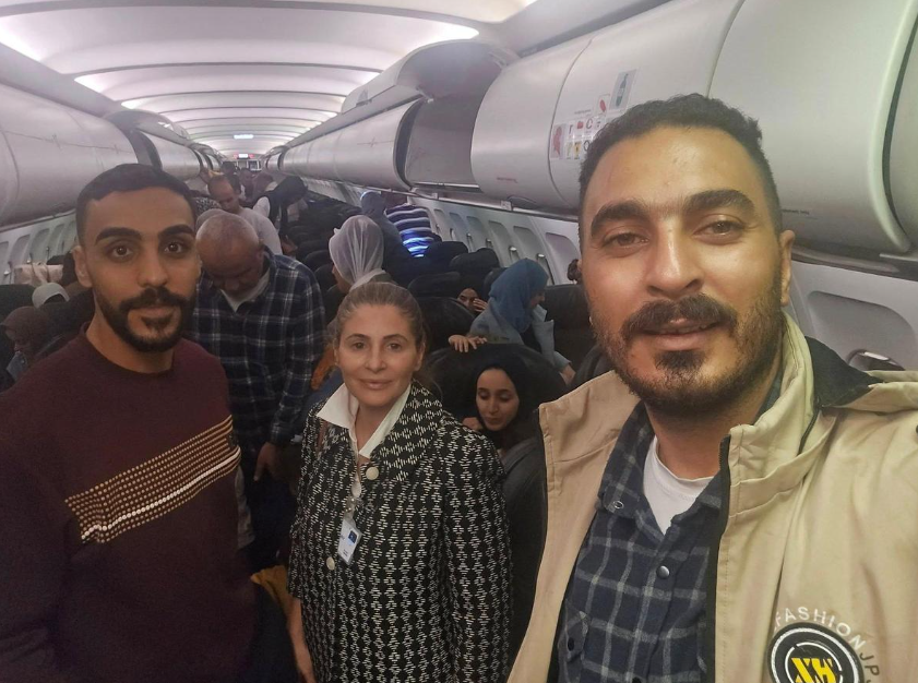 Palestinian passengers sit on a plane with hands raised, arriving in South Africa amid controversy over charter flights from Gaza