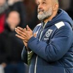 Nuno Espirito Santo smiling and holding a West Ham home shirt during his appointment as manager, standing in front of a sponsors board