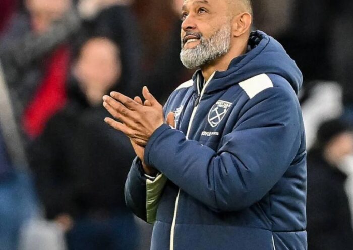 Nuno Espirito Santo smiling and holding a West Ham home shirt during his appointment as manager, standing in front of a sponsors board