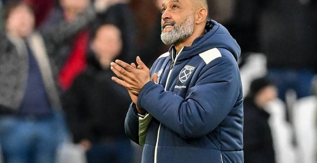 Nuno Espirito Santo smiling and holding a West Ham home shirt during his appointment as manager, standing in front of a sponsors board