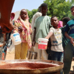 Volunteers in Sudan ladle food from large containers in a community kitchen, providing meals to people affected by war and famine.