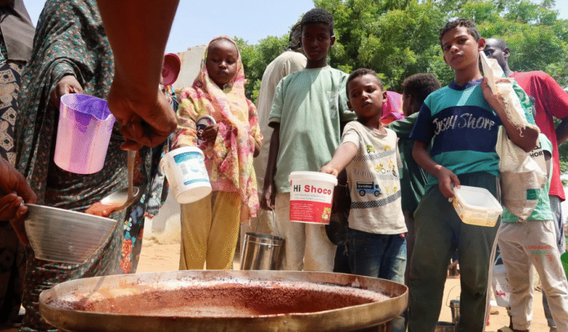 Volunteers in Sudan ladle food from large containers in a community kitchen, providing meals to people affected by war and famine.