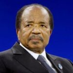 Cameroon President Paul Biya holding his swearing-in certificate during the inauguration ceremony in Yaoundé, wearing a dark suit in front of microphones