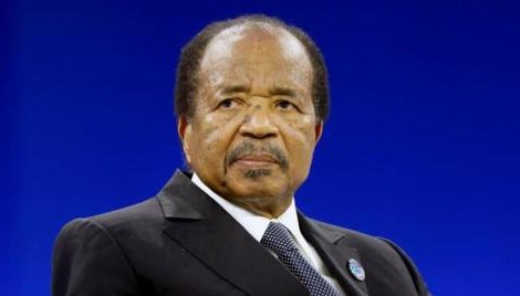 Cameroon President Paul Biya holding his swearing-in certificate during the inauguration ceremony in Yaoundé, wearing a dark suit in front of microphones