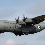 Nigerian Air Force C-130 aircraft on a dimly lit runway at night, illuminated by orange lights.