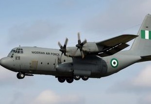 Nigerian Air Force C-130 aircraft on a dimly lit runway at night, illuminated by orange lights.
